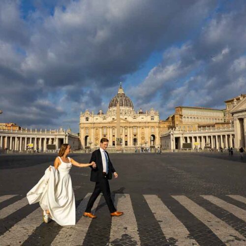 Pair crossing Via della Conciliazione hand in hand, with St. Peter’s Basilica in the distance forming the backdrop for this Rome street photograph