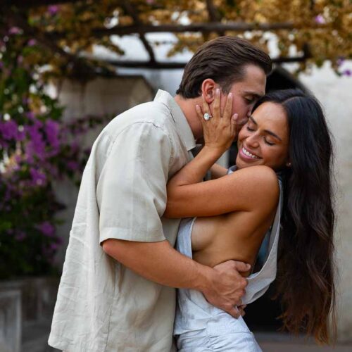 A smiling couple portrait framed by vibrant bougainvillea flowers during a twilight engagement session in Ravello.