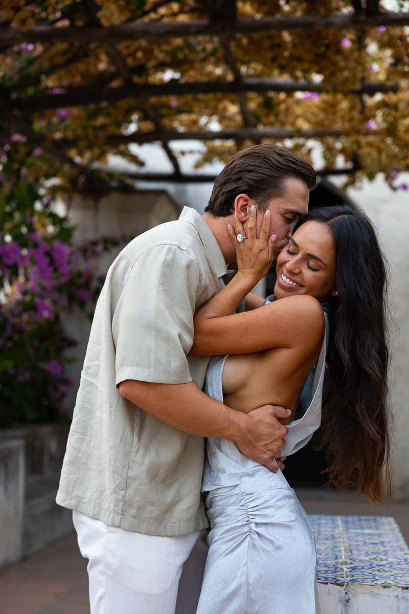 A smiling couple portrait framed by vibrant bougainvillea flowers during a twilight engagement session in Ravello.