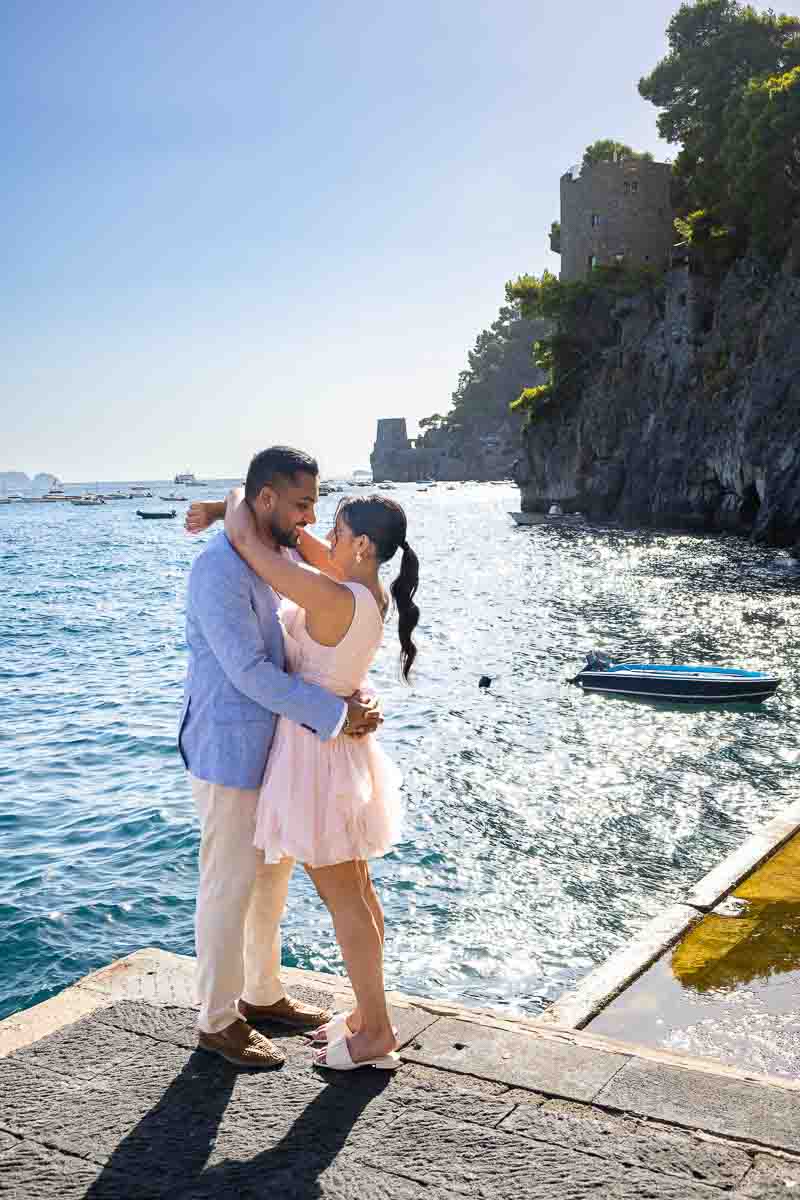 Full-figure landscape imagery of a pair standing by the marina with a historic Saracen tower.