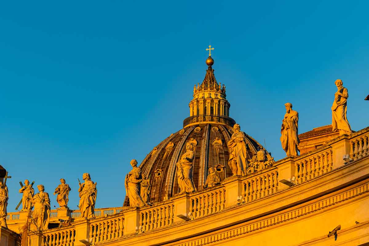 Close-up details of the stone angel statues lining the monumental travertine roof wall above the grand architectural columns.