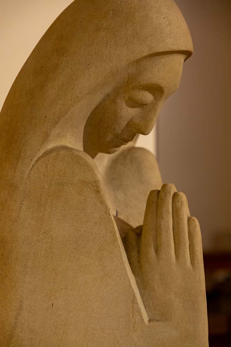 Detailed profile shot of a marble religious figure with folded hands in silent devotion and prayer