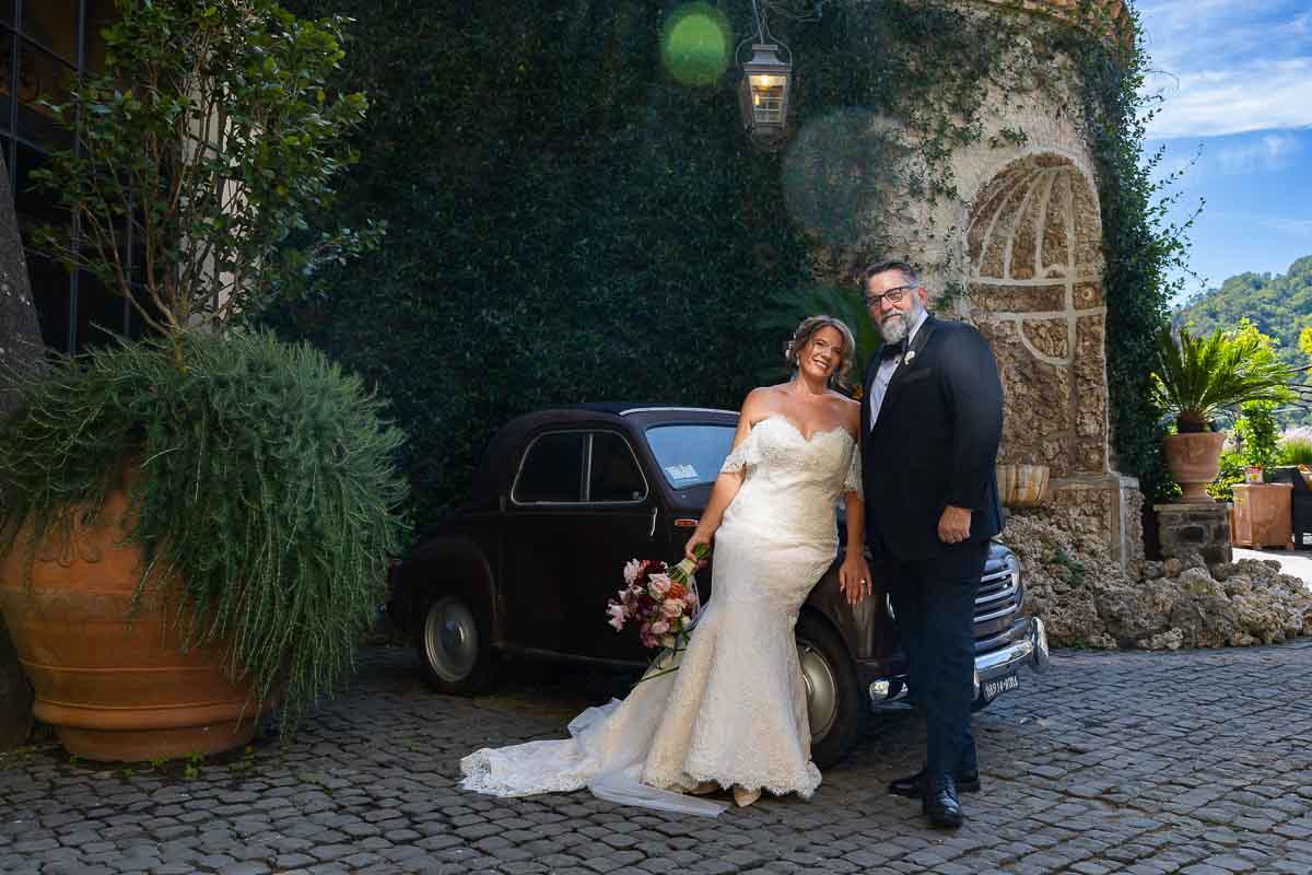 The bride and groom posing for photos alongside a classic vintage car on the venue property.