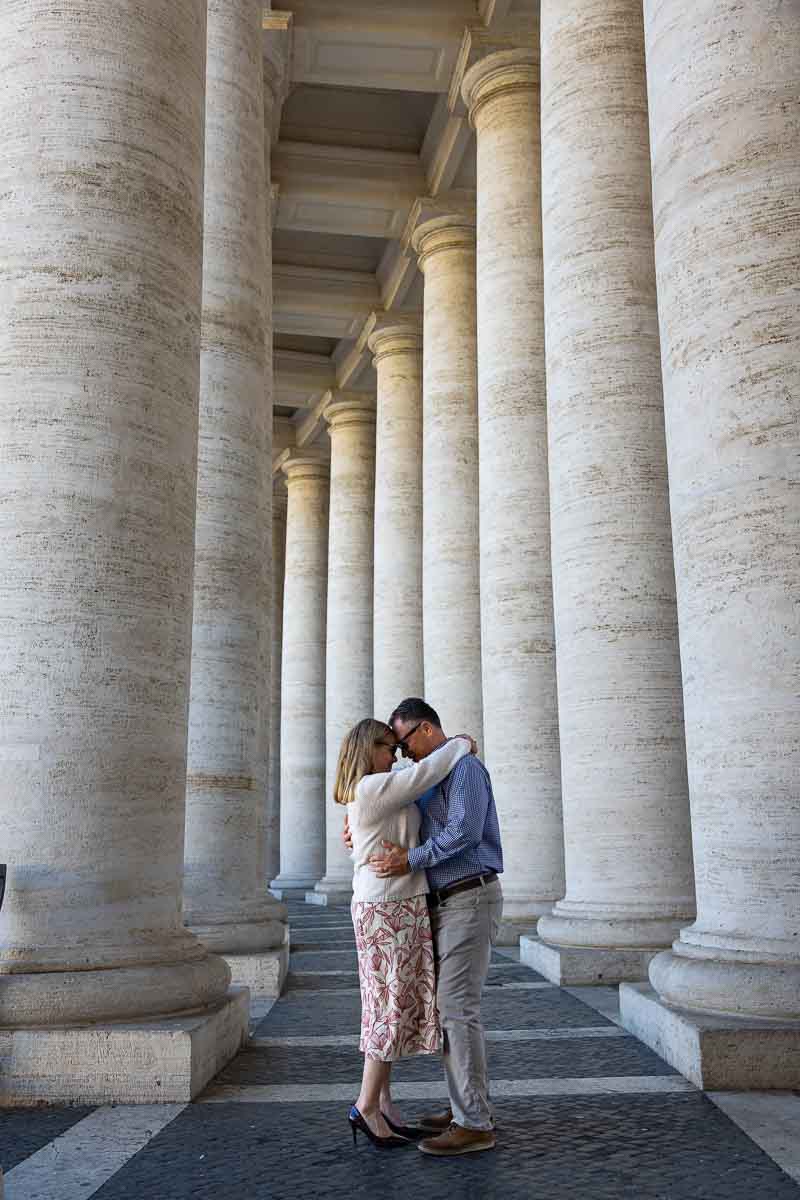 Artistic architectural framing of a relaxed pair during a professional photographer session among the massive curved travertine pillars enclosing the historic grand piazza