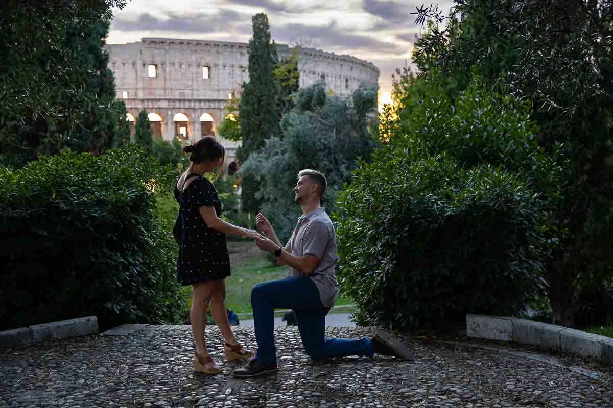 A romantic marriage request showing the partner on one knee before the majestic Colosseum at sunset.