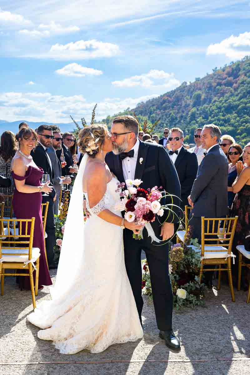 A wide-angle perspective of the marital kiss with cheering guests in the background.