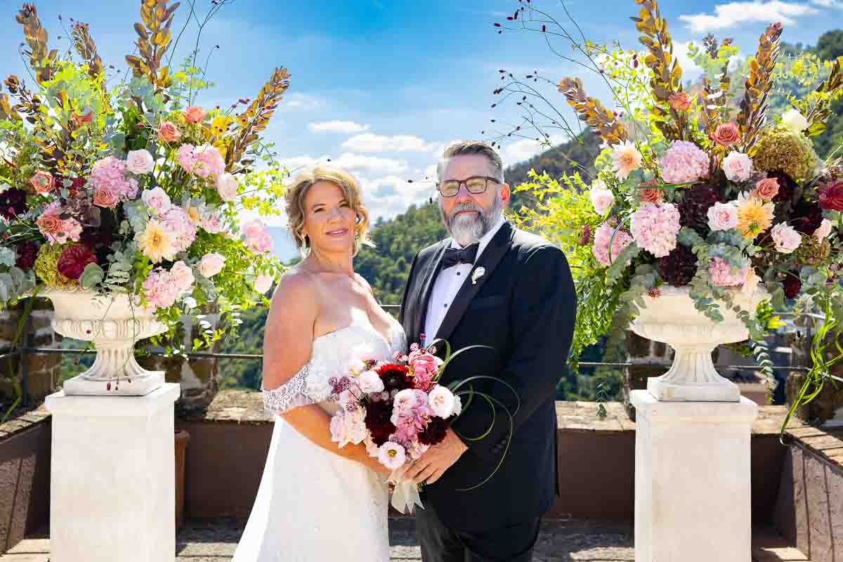 The romantic couple posing together for unique and creative photography amidst towering floral arrangements on the terrace.