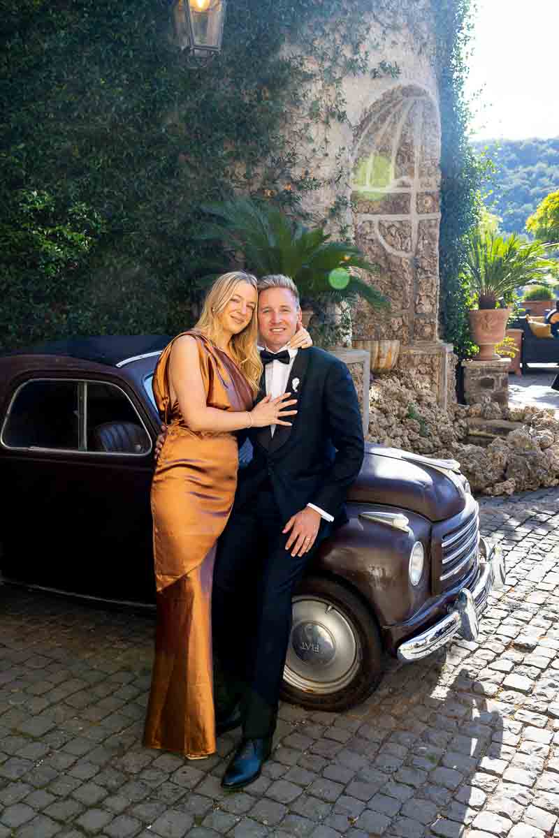 Couple posed photoshoot while leaning on a vintage classic Italian car during wedding day coverage