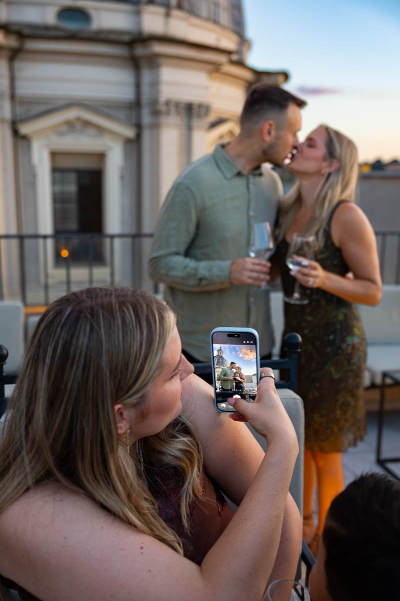 The couple kissing while a guest takes a quick photo of them with a mobile phone.