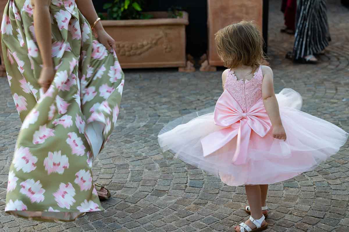 A young flower girl playfully spinning her gown dress around in the courtyard.