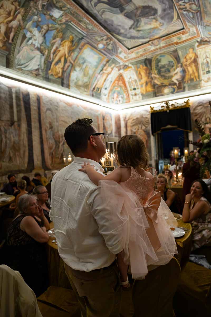 A candid photo capturing an elegant dinner guest enjoying the festive evening atmosphere. Surrounded by ancient alfresco paintings on the wall and celling